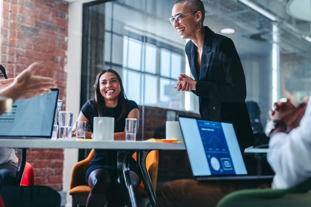 Young businesswoman receiving praise from her colleagues during a meeting in a modern office. Successful young businesswoman smiling cheerfully while being acknowledged by her team.